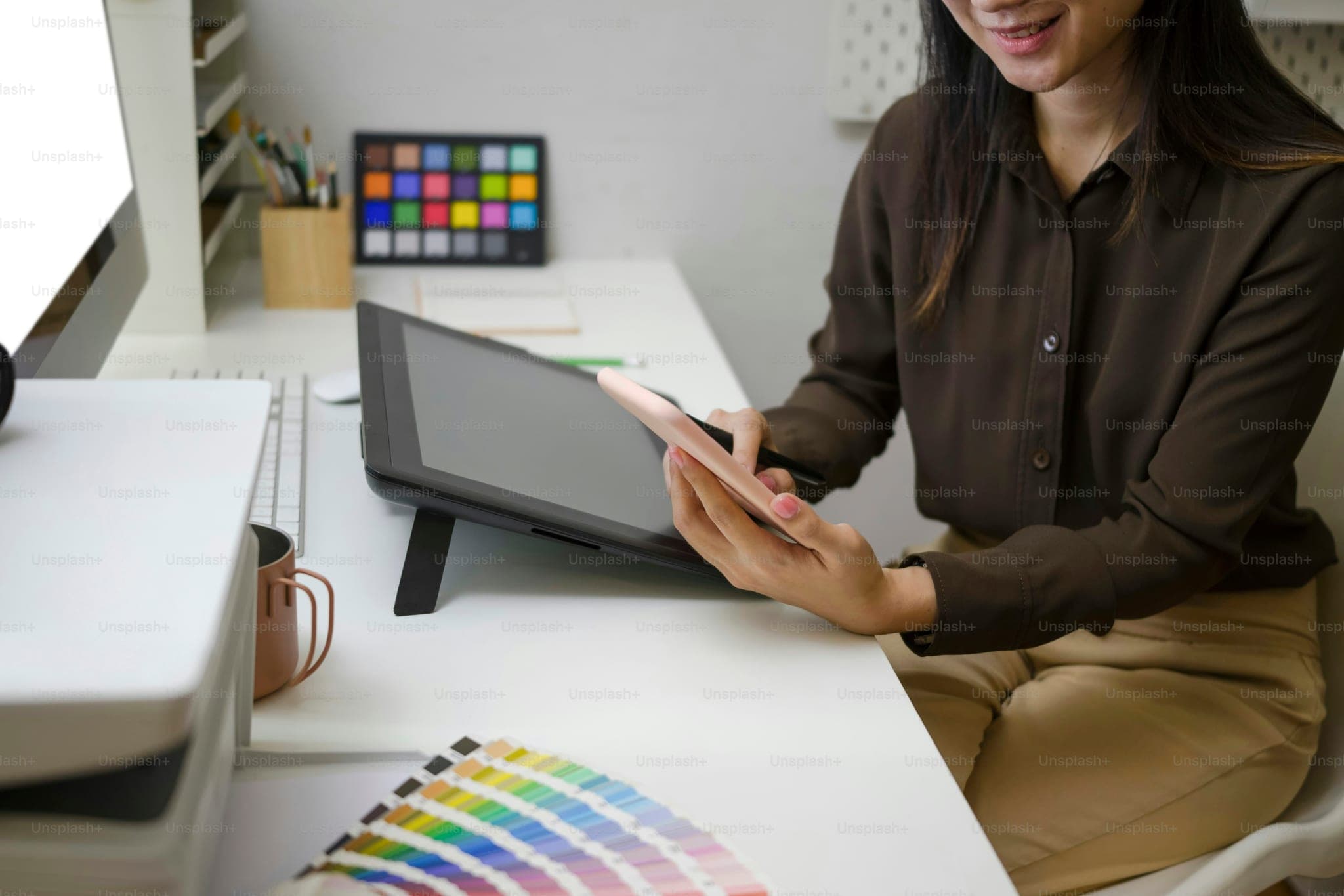 Cropped shot of smiling female graphic designer sitting at her workplace and using mobile phone for texting or massaging with her friends.